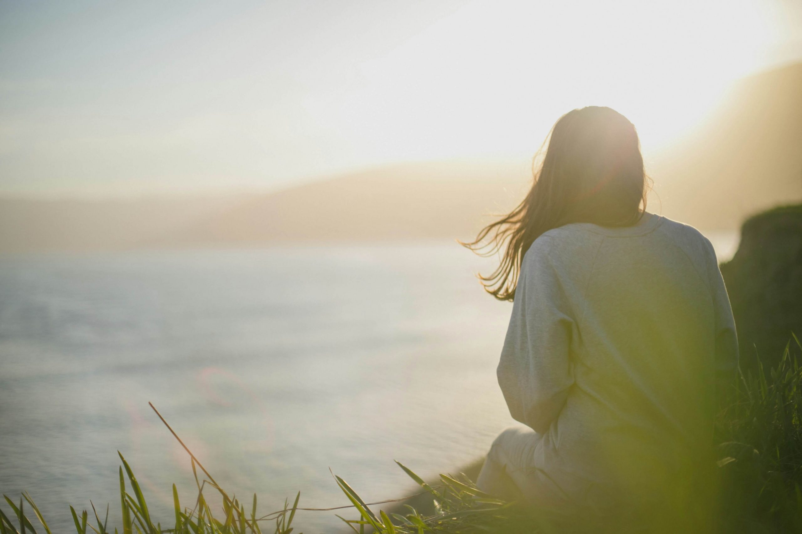 Image of a woman sitting on the ground looking at a body of water as the sun sets. Begin healing from your depression symptoms with depression counseling in Englewood, CO.