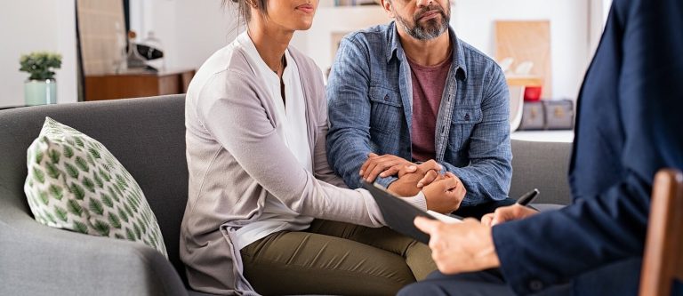 A couple holds hands while sitting across from a person with a clipboard. This could represent the support a couples therapist in Englewood, CO can offer for relationships. Learn more about couples therapy in Littleton, Co and relationship counseling in Englewood, CO today.