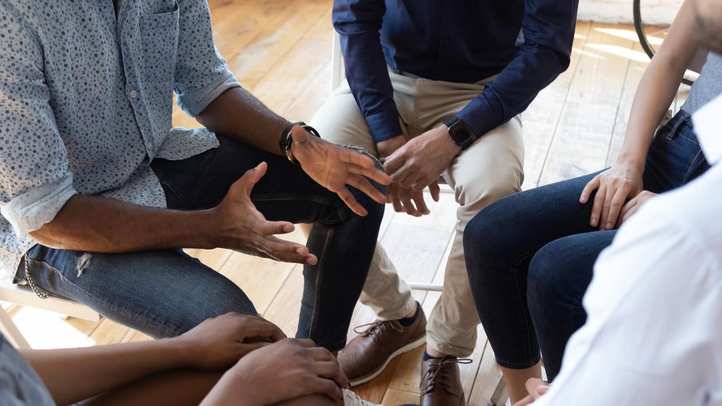 A close up of a group talking while sitting in a circle. Learn how family therapy in Englewood, CO can offer support with addressing issues. Search for online therapy in Colorado to get in touch with a family therapist in Englewood, CO today.