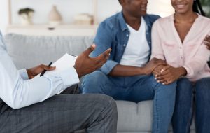 A couple smiles while sitting across from a person with a clipboard. This could represent the support a family therapist in Englewood, CO can offer. Search for family therapy in Englewood, CO to learn more about online therapy in Colorado and other services. 